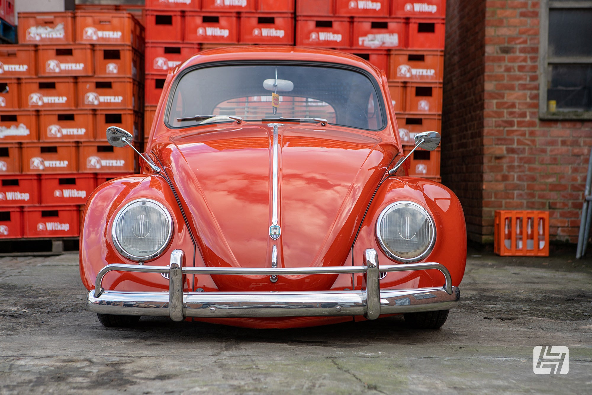 Orange VW Beetle front end with Swan Neck mirrors and chrome US spec towel rail bumpers photographed in front of beer crates at Witkap brewary 