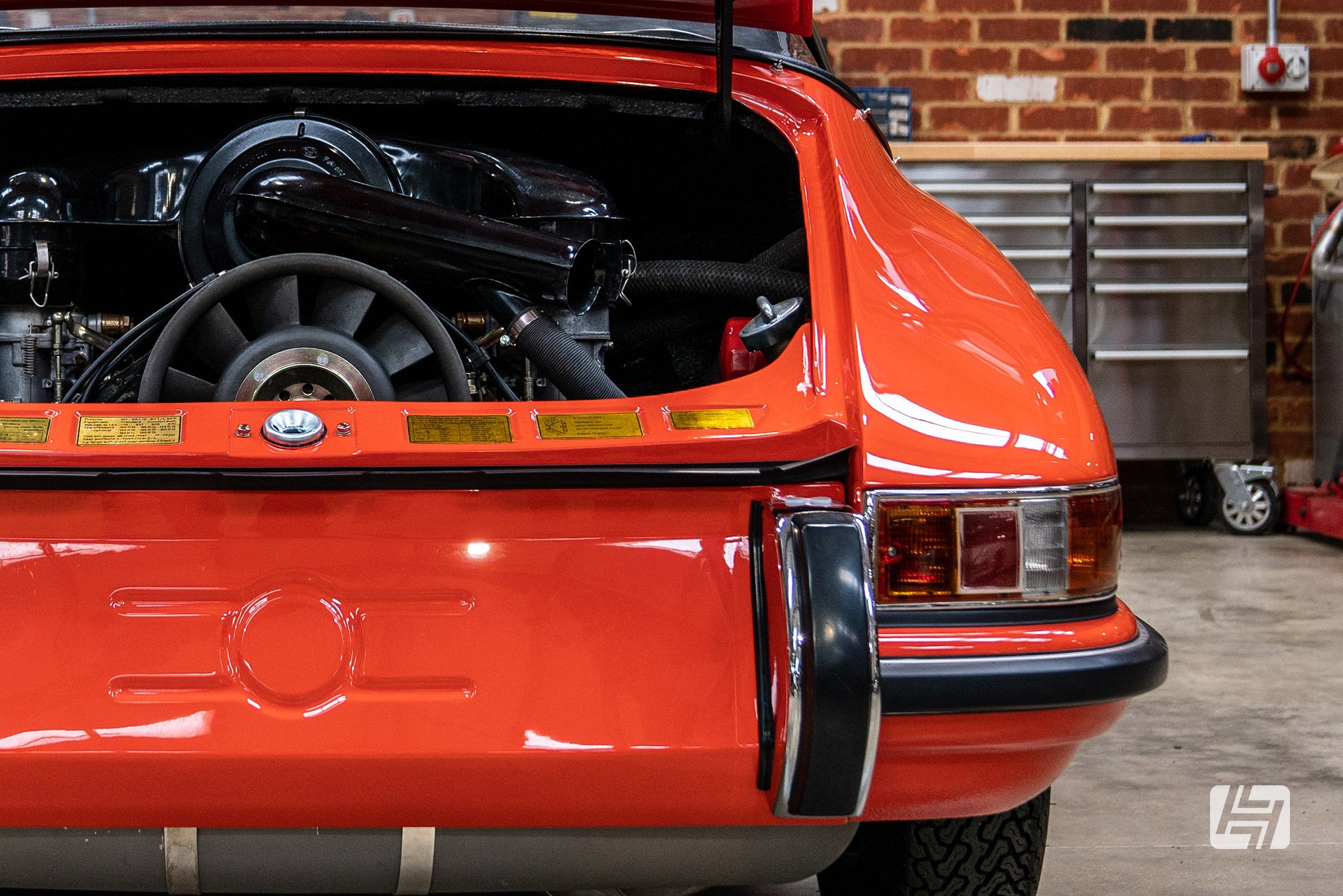 Orange Porsche 911 rear with engine lid open and pressing behind number plate visible